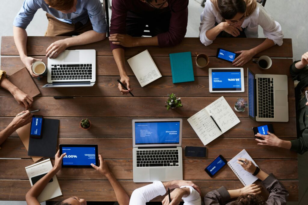 A group of professionals collaborating around a table with laptops and tablets, discussing IT services and business strategy.