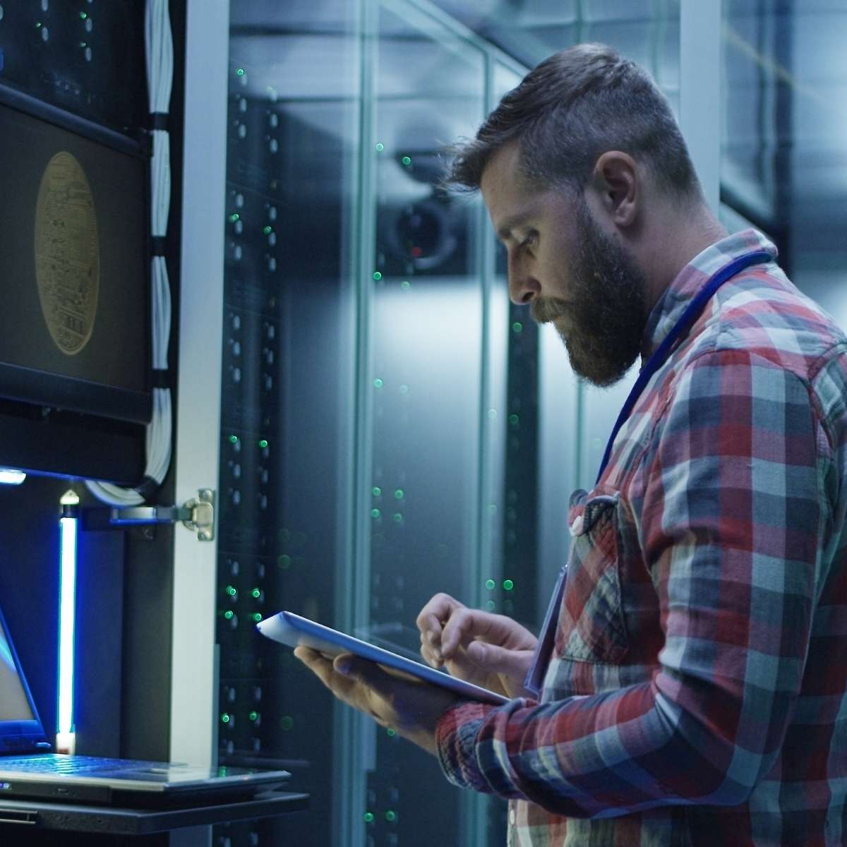 Technician standing and working in a data center, surrounded by rows of server racks and networking equipment, representing hands-on infrastructure management and maintenance.